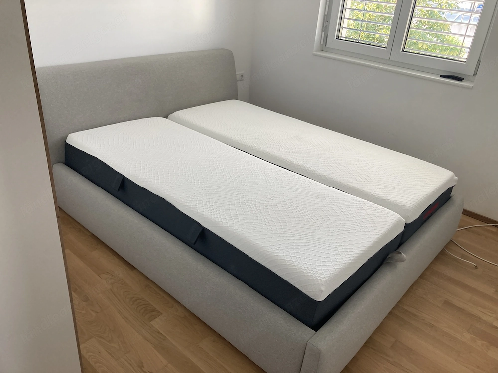 Schönes, gemütliches Bett mit grauem Stoffbezug